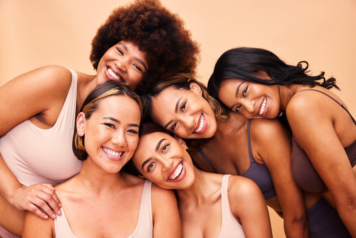 Five women standing closely together, smiling, against a solid light-colored background