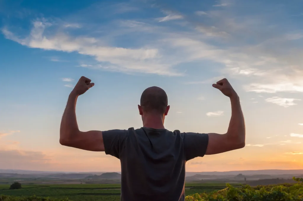 Man seen from behind flexing his arms outdoors at sunset