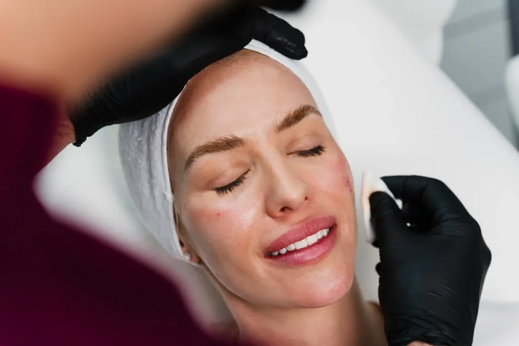 Woman with closed eyes receiving a facial treatment from gloved hands