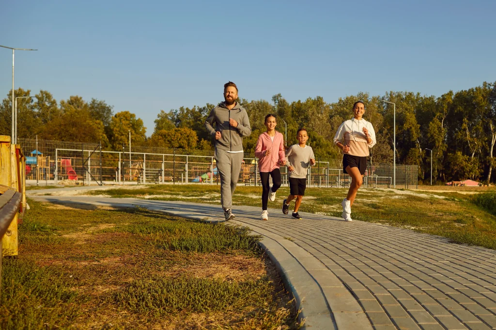 Family of four jogging together on a paved path in a park during daylight