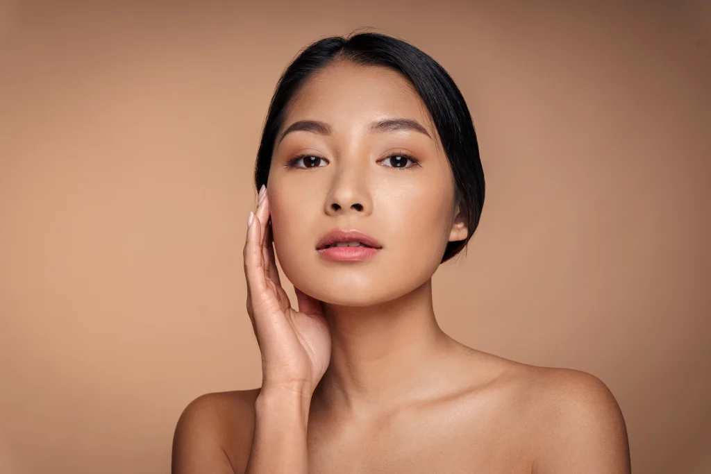 Woman with smooth skin touching her cheek against a neutral beige background