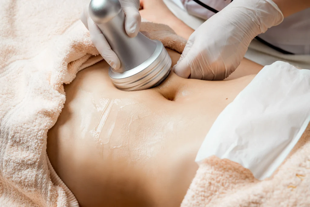 Practitioner uses a handheld body contouring device on the abdomen with clear gel applied to the skin.
