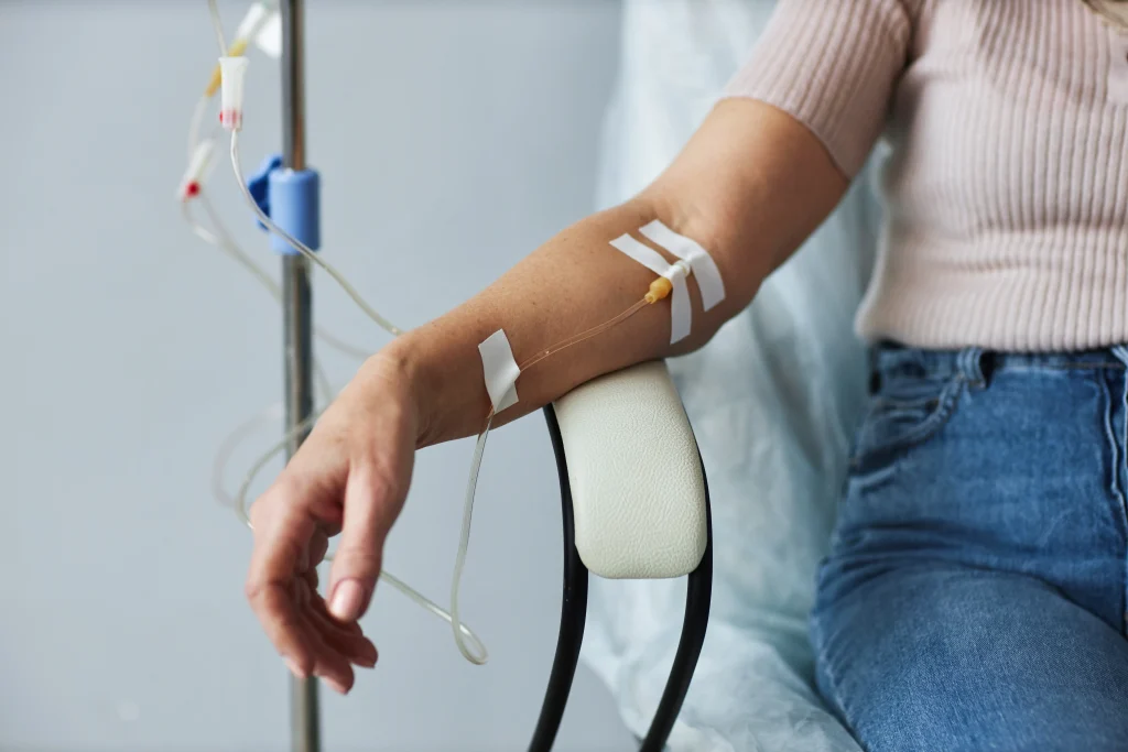 Person receives IV therapy through an arm infusion while seated beside an IV stand.