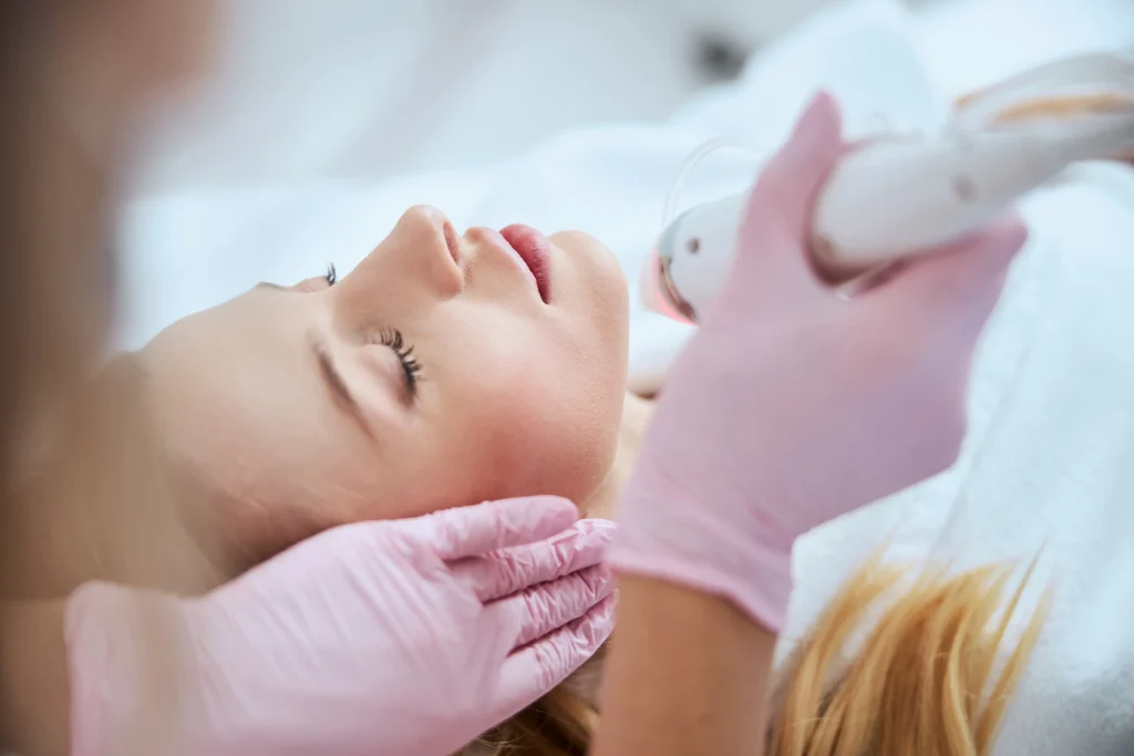 Practitioner performs a microneedling facial treatment while supporting the patient's head with gloved hands.