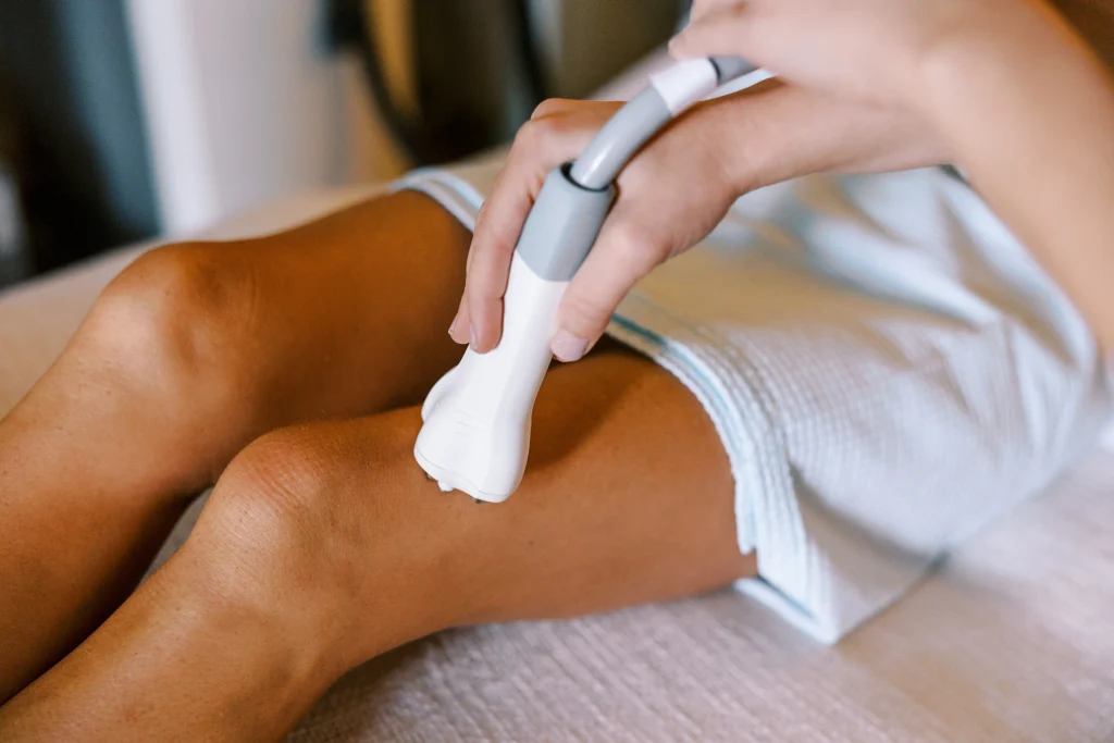 Practitioner uses a handheld body contouring device on a patient's thigh during a treatment session.